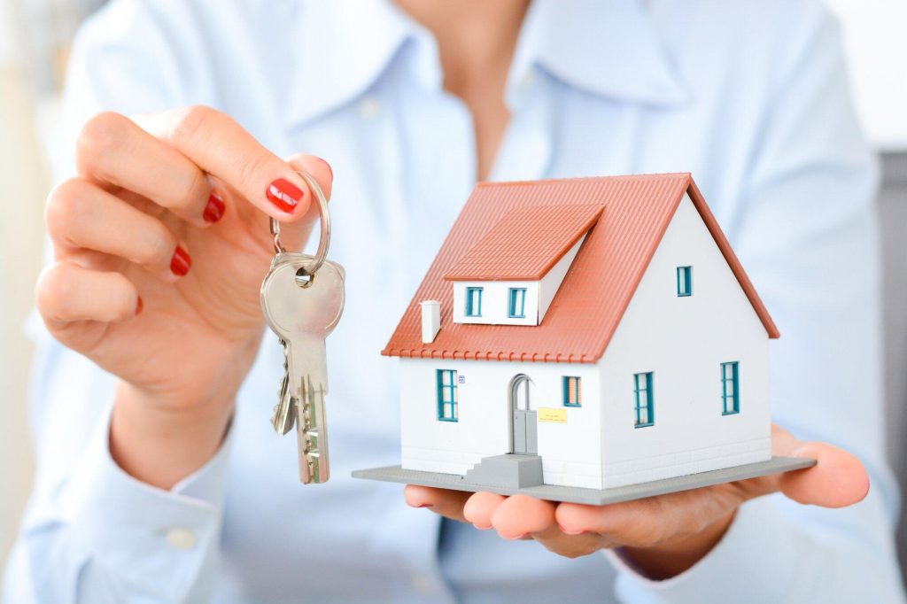 real estate agent holding a set of keys in one hand and a mini house model in the other hand